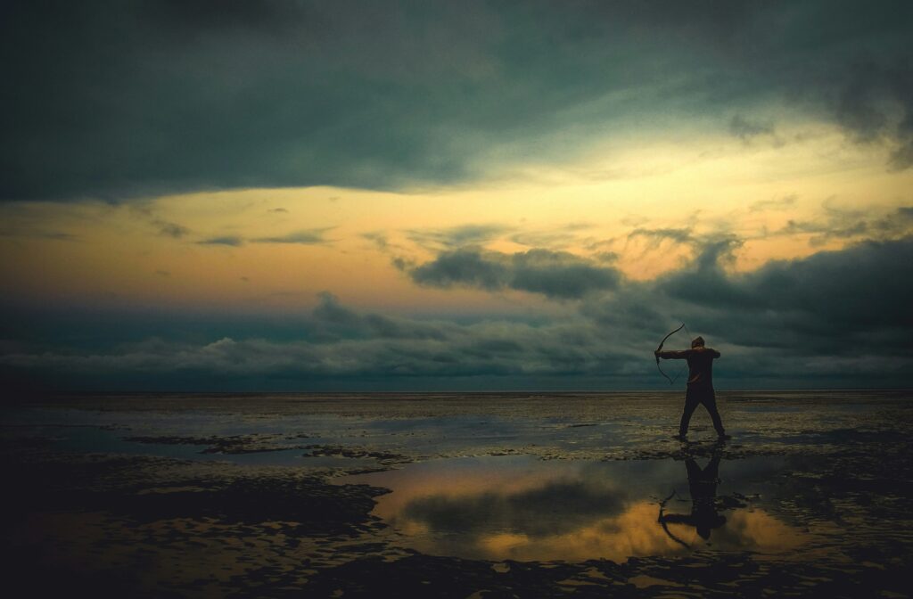 Un uomo con un arco su una spiaggia riflettente al tramonto simboleggia il peccato di seguire un bersaglio imposto e la ricerca interiore di una direzione autentica. L’atmosfera suggestiva evoca solitudine, riflessione e il conflitto tra destino e scelta personale. Un uomo con un arco su una spiaggia riflettente al tramonto simboleggia il peccato di seguire un bersaglio imposto e la ricerca interiore di una direzione autentica. L’atmosfera suggestiva evoca solitudine, riflessione e il conflitto tra destino e scelta personale.